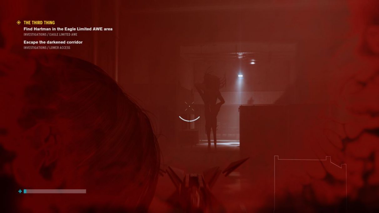 Una captura de pantalla del DLC Control AWE que muestra al gran malvado Hartman, una forma indistinta acechando justo frente a una luz.  Sus proporciones son las de un humano, pero como si hubiera sido estrujado y estirado, por lo que sus brazos y piernas son anormalmente largos. 