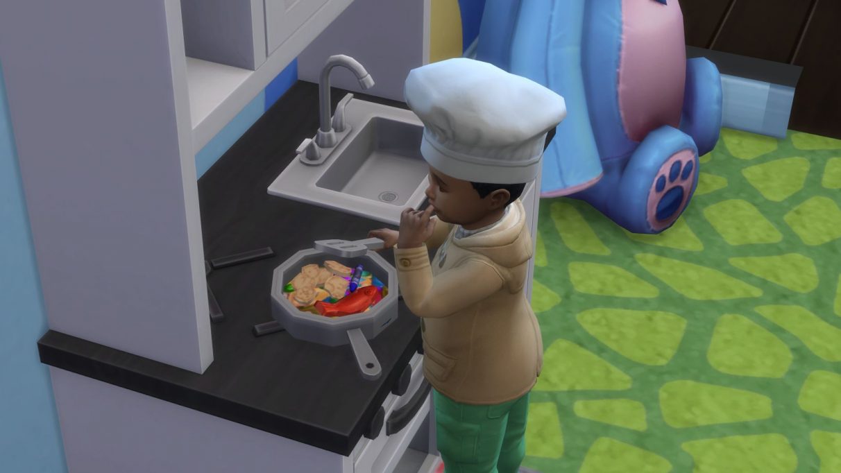 Una captura de pantalla de un niño pequeño que usa la cocina de juegos de contenido personalizado en Los Sims 4. Está revolviendo una sartén llena de crayones y otros juguetes pequeños, y se ha llevado un dedo a los labios como para probar el sabor.  Lleva un pequeño gorro de cocinero.